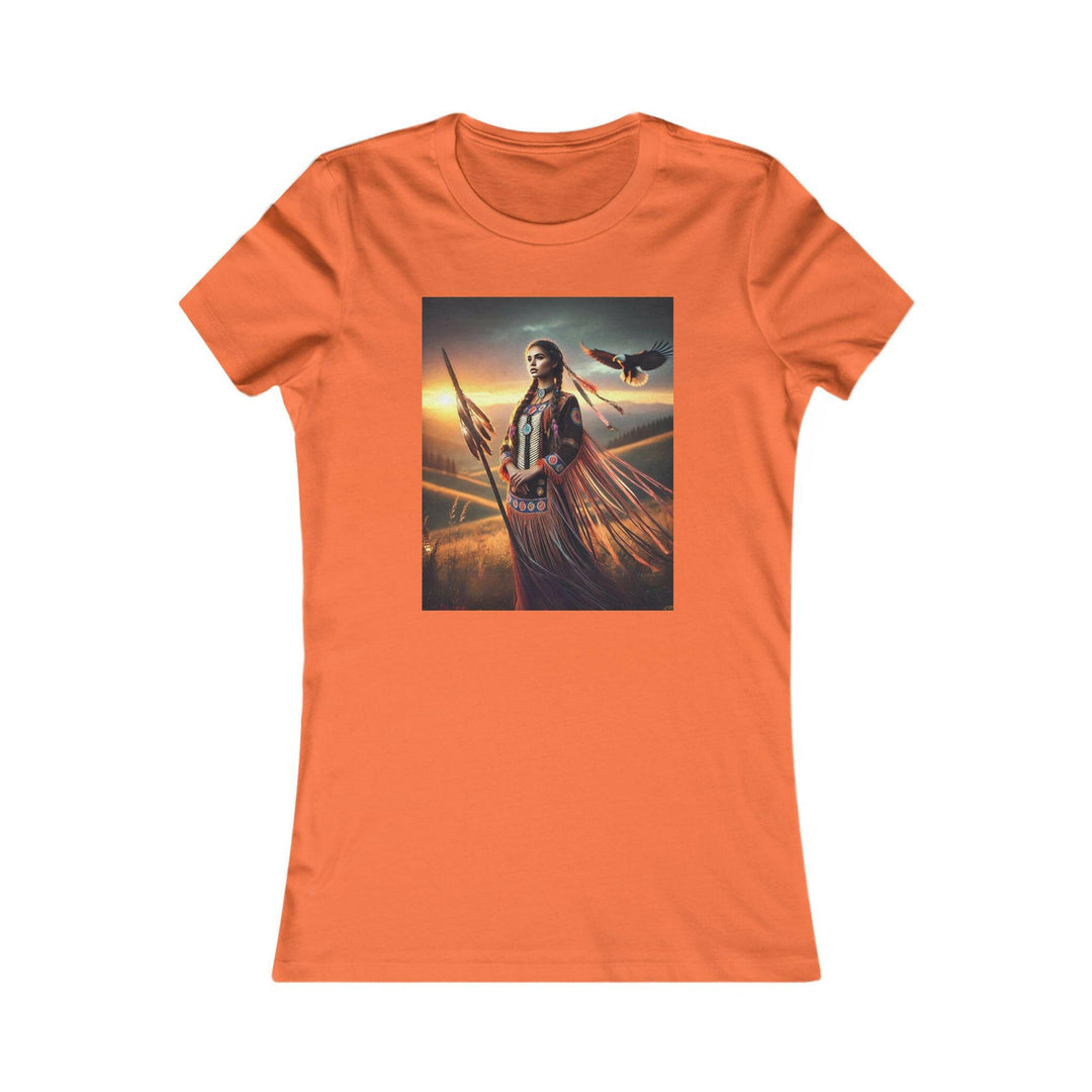 Orange T-shirt featuring an illustration of a Native American warrior woman with a spear, set against a dramatic sunset. Represents strength, heritage, and cultural pride.