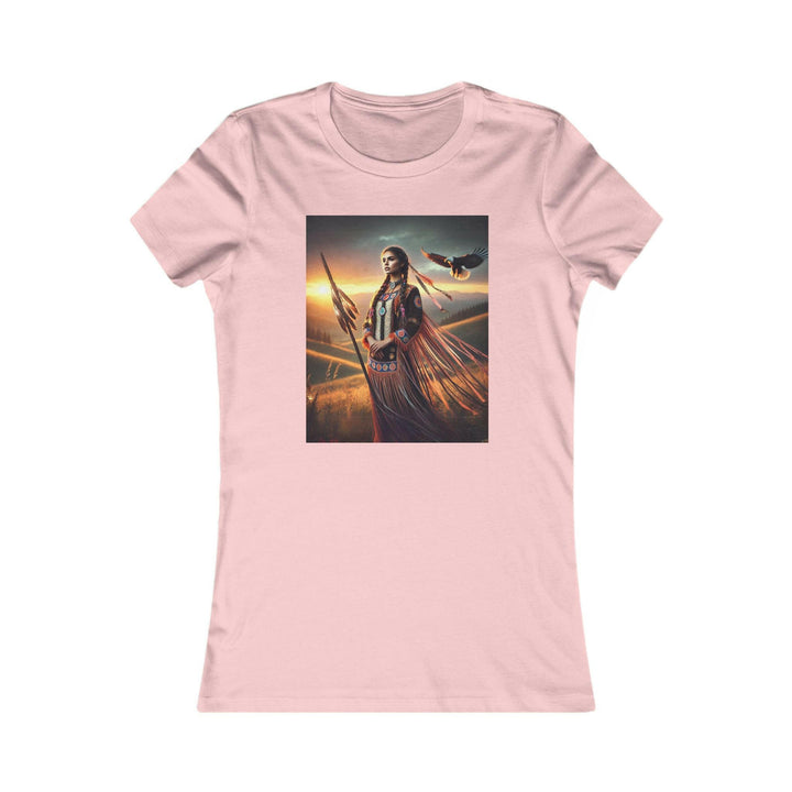 Pink T-shirt featuring an illustration of a Native American warrior woman with a spear, set against a dramatic sunset. Represents strength, heritage, and cultural pride.